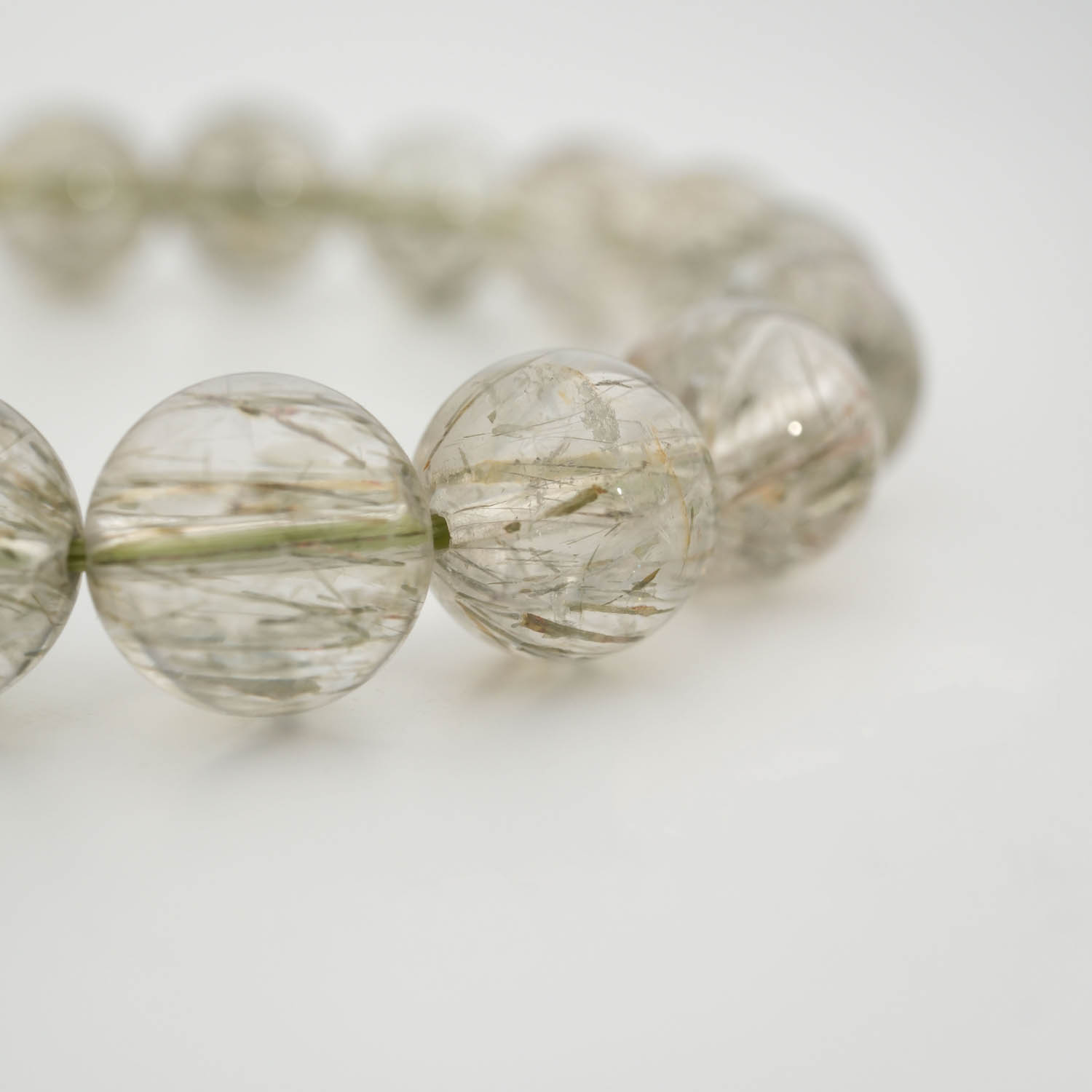 سوار-حجر-طبيعي-كوارتز-روتيلي-أخضر-أصلي A luxury flexible natural stone bracelet made of 11-12mm round smooth clear quartz beads with sharp green rutilated inclusions.