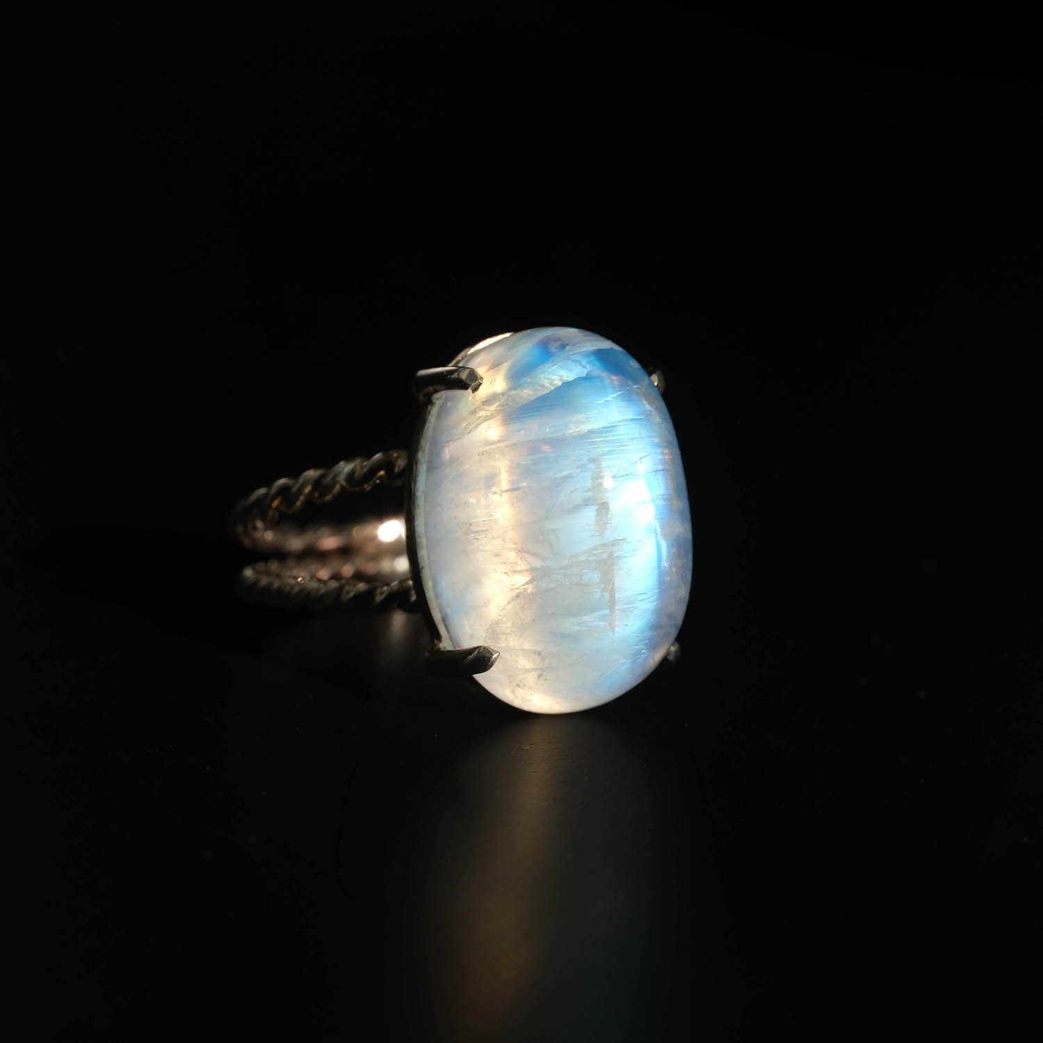 anillo-diseno-lujo-mujer-piedra-de-luna-natural-plata-925-trenzado Anillo de diseño de lujo para mujer en plata de ley 925 con banda trenzada, adornado con una gran gema de piedra de luna natural de reflejo azul.