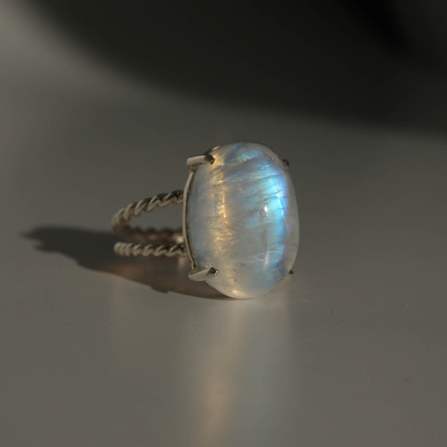 bague-luxe-femme-pierre-de-lune-naturelle-argent-925-torsade Bague de luxe pour femme en argent sterling 925 avec anneau torsadé, ornée d'une grande pierre de lune naturelle originale à reflet bleu.