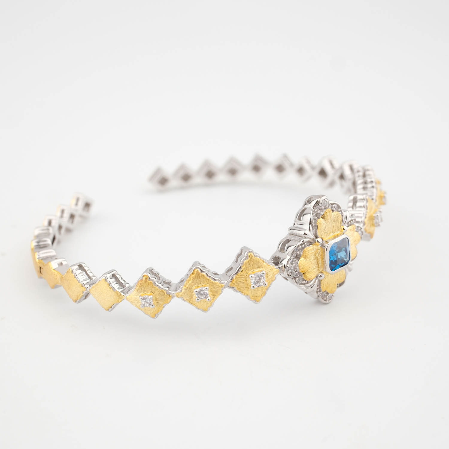 bracciale-rigido-argento-925-stile-barocco-lusso-blu A luxury designer bangle bracelet featuring a square faceted blue gemstone surrounded by textured gold plated baroque details in 925 sterling silver.