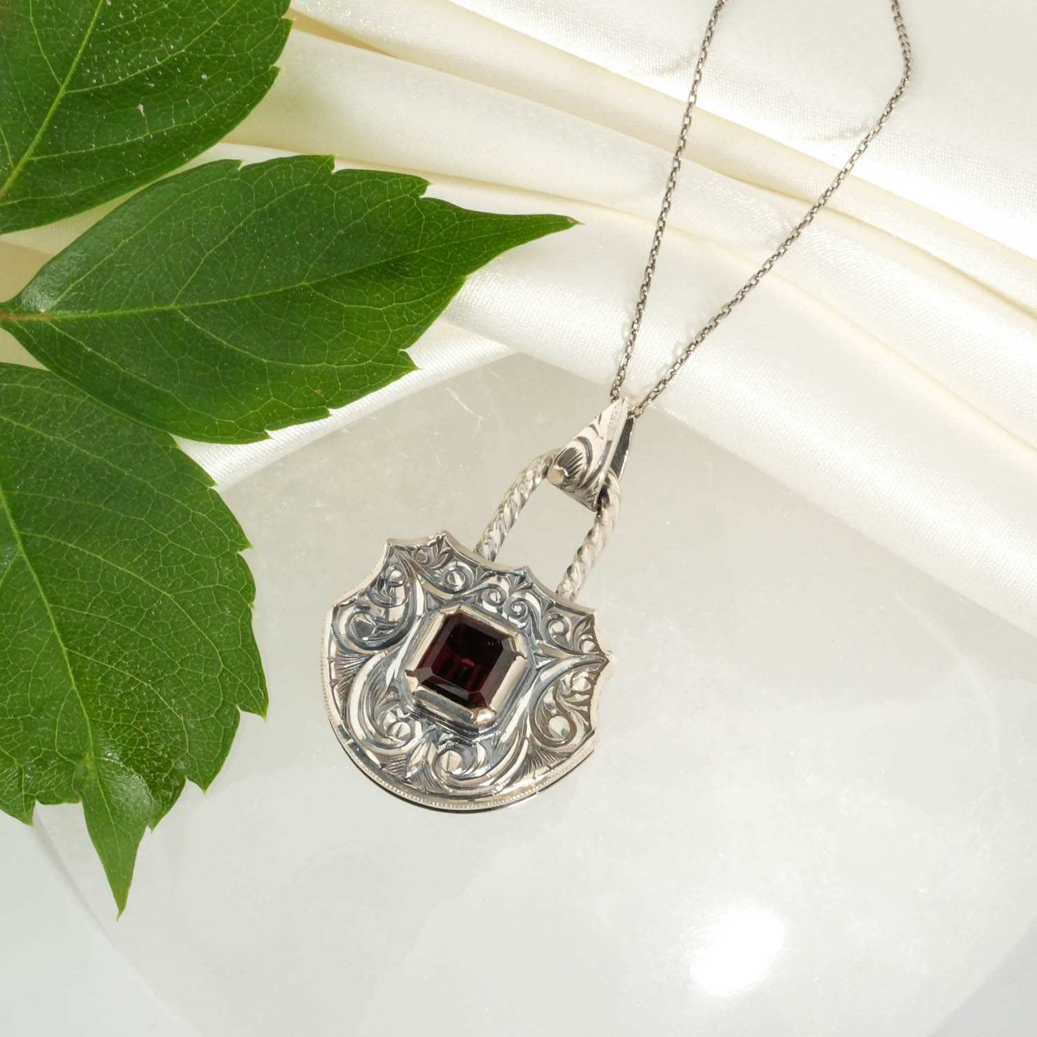 garnet-lal-tasi-kilit-tasarim-kalem-iscilikli-925-ayar-gumus-kolye Orijinal doğal garnet lal taşı baget kesim kilit tasarım el oyması kalem işçilikli 925 ayar oksitli gümüş kolye.