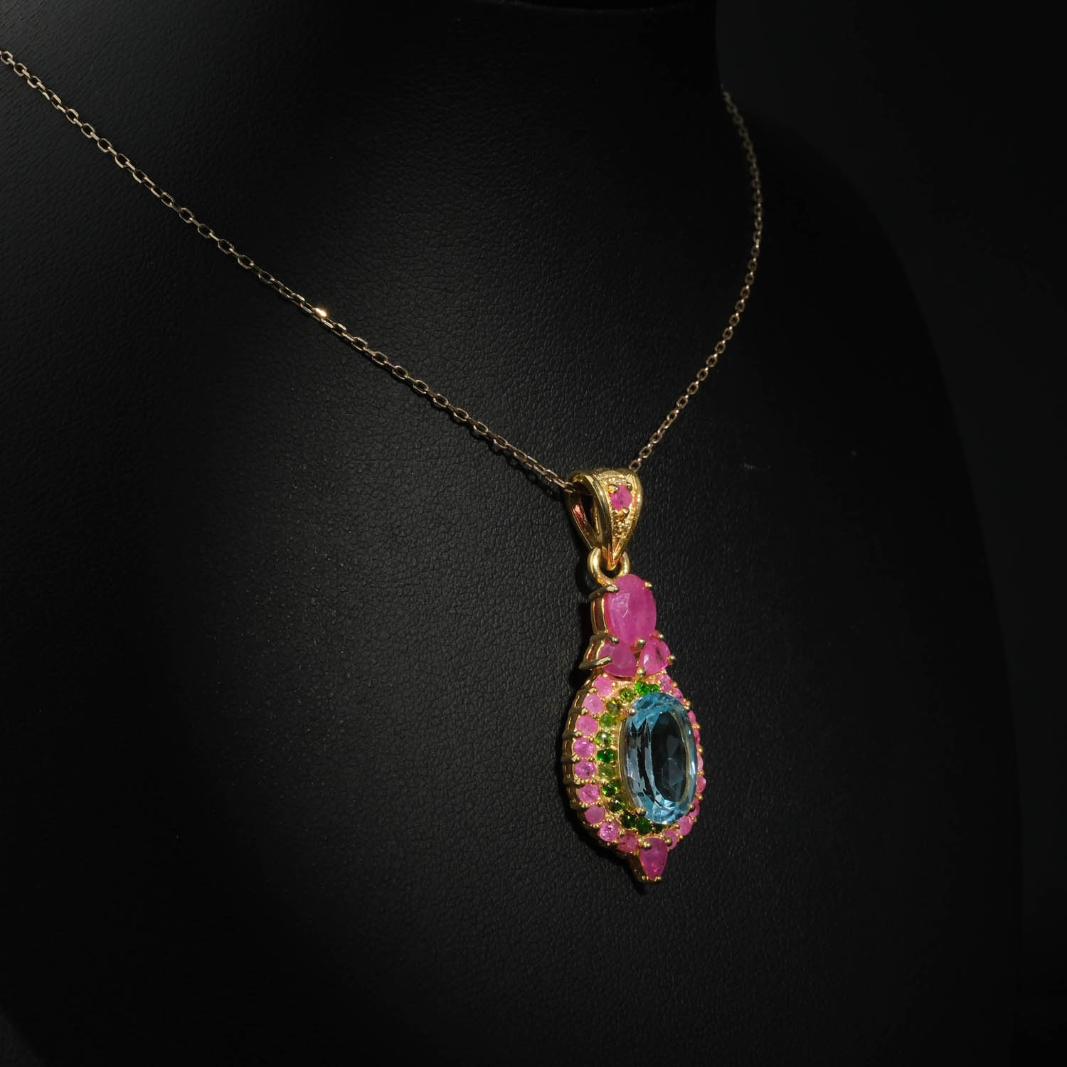 collier-femme-topaze-bleue-rubis-tsavorite-argent-dore.jpg Collier médaillon royal pour femme avec topaze bleue naturelle, rubis et tsavorite en argent 925 plaqué or sur satin blanc.