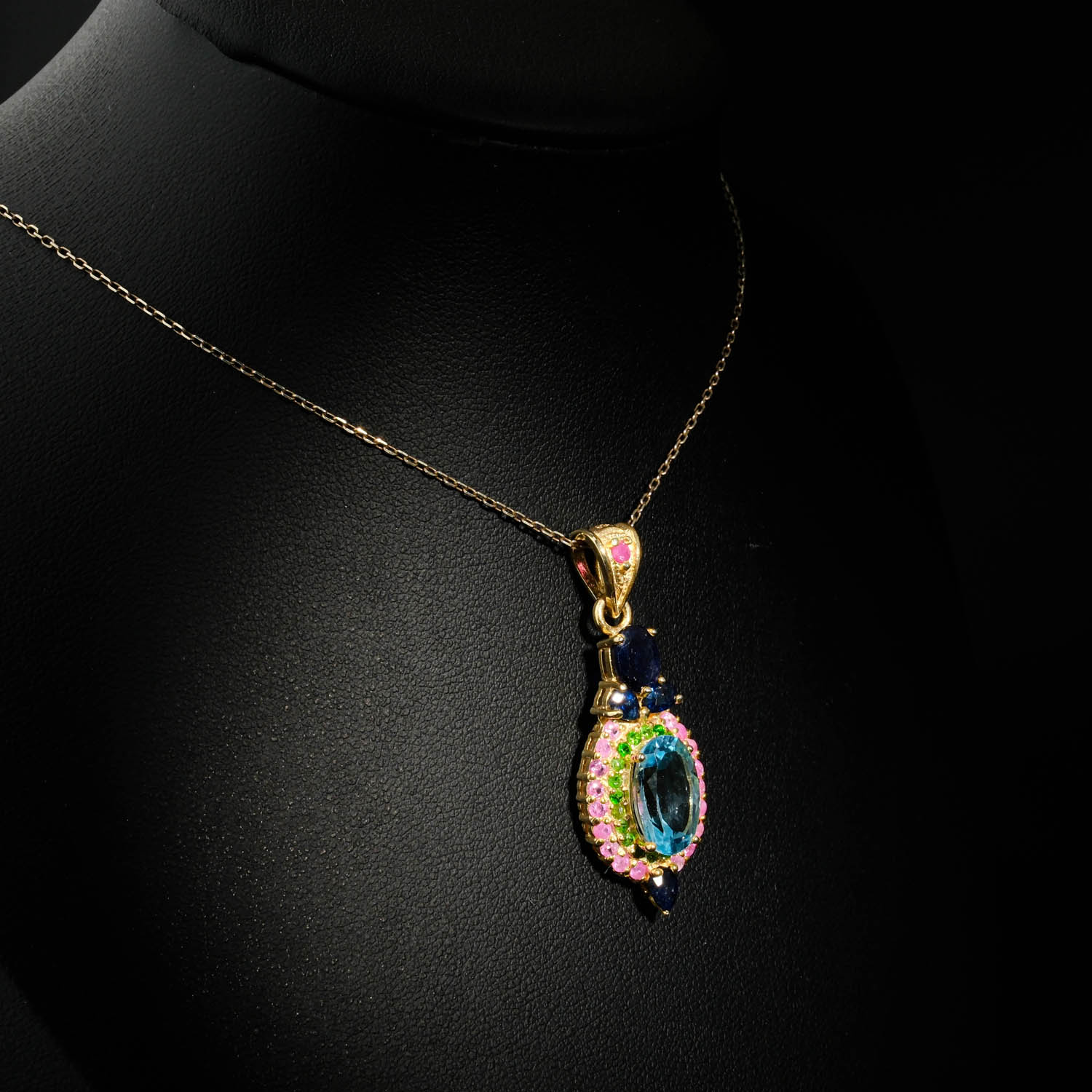 collier-femme-topaze-bleue-saphir-rubis-tsavorite-argent-dore.jpg Collier médaillon royal pour femme avec topaze bleue naturelle, saphirs bleus, rubis et tsavorite en argent 925 plaqué or sur satin blanc.