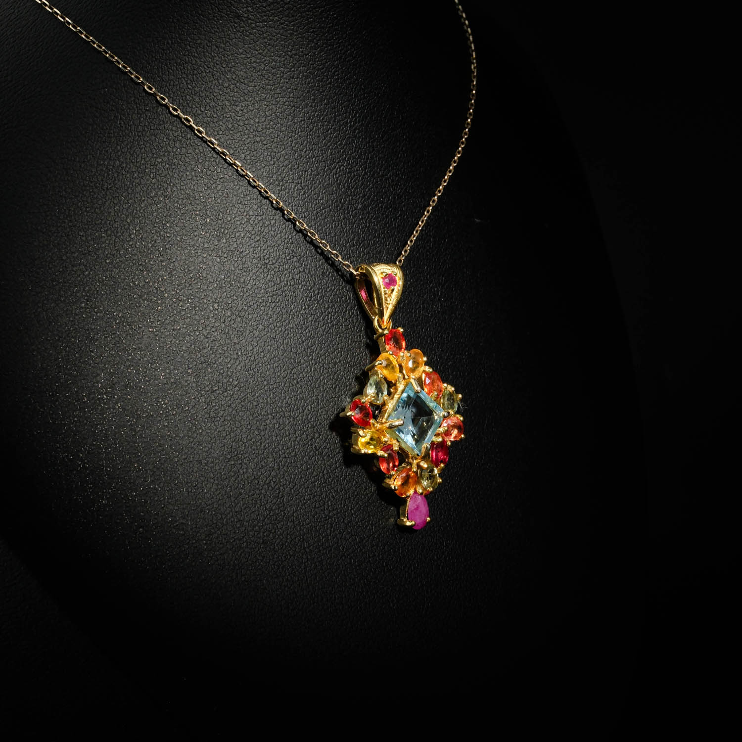 collier-femme-topaze-bleue-saphirs-colores-rubis-argent-dore.jpg Collier médaillon royal pour femme avec topaze bleue carrée, saphirs multicolores et rubis en argent 925 plaqué or sur satin blanc.