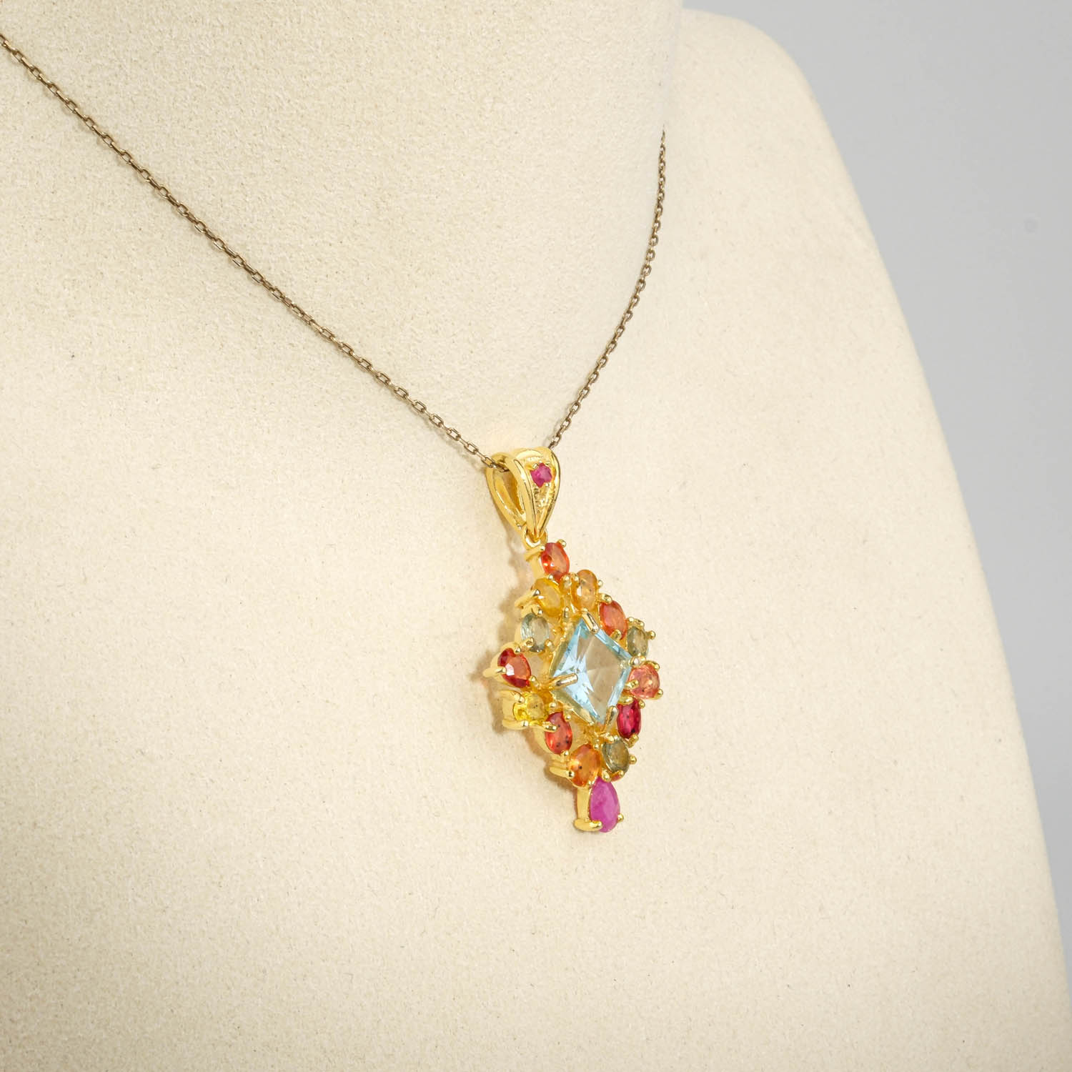 damen-kette-925-silber-gold-blauer-topas-bunte-saphire-rubin.jpg Damen Anhänger Kette aus 925 Silber vergoldet mit blauem Topas im Quadratschliff, bunten Saphiren und Rubin auf weißer Seide.
