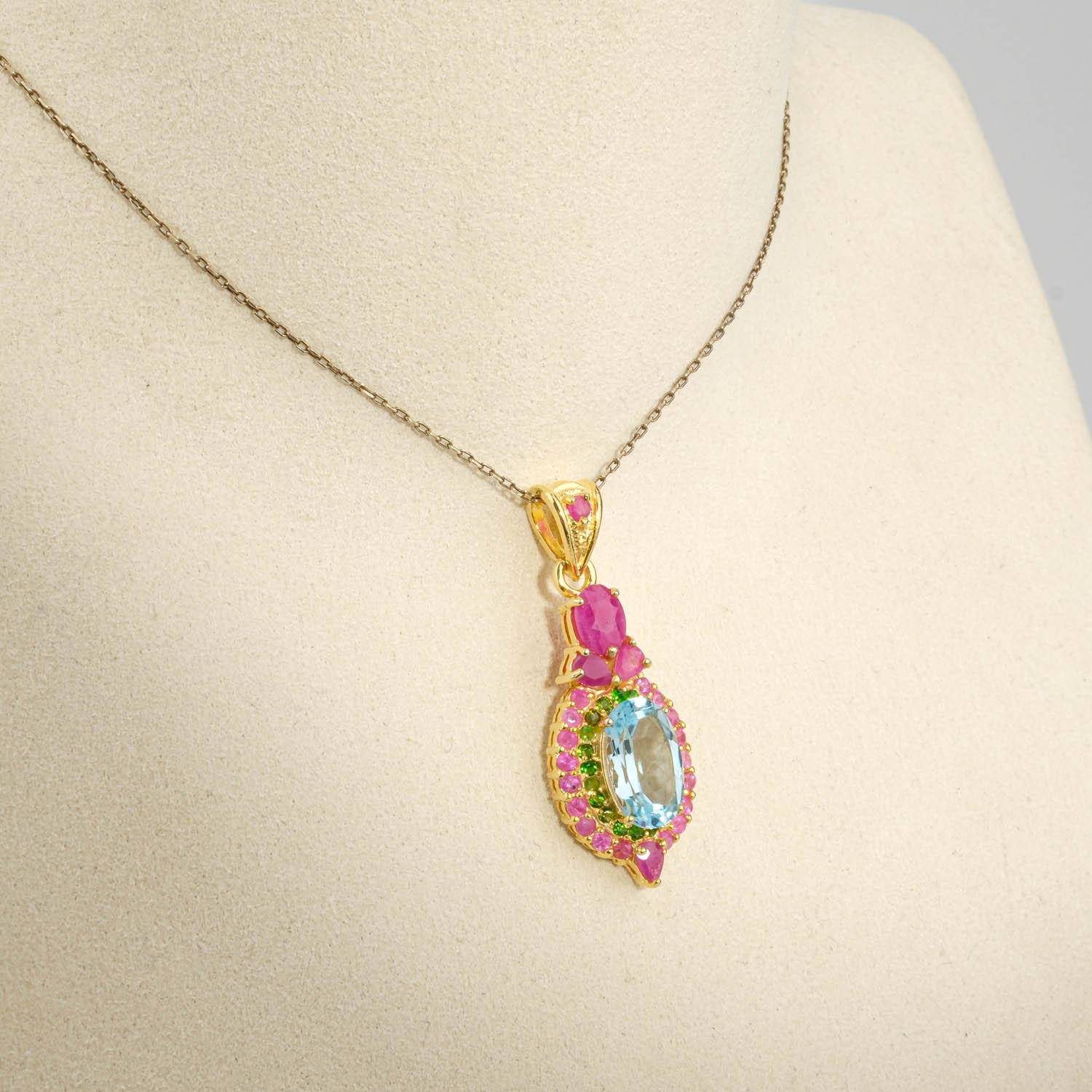 damen-kette-925-silber-gold-blauer-topas-rubin-tsavorit.jpg Damen Anhänger Kette aus 925 Silber vergoldet mit facettiertem blauem Topas, Tsavorit und Rubin-Kranz auf weißer Seide.