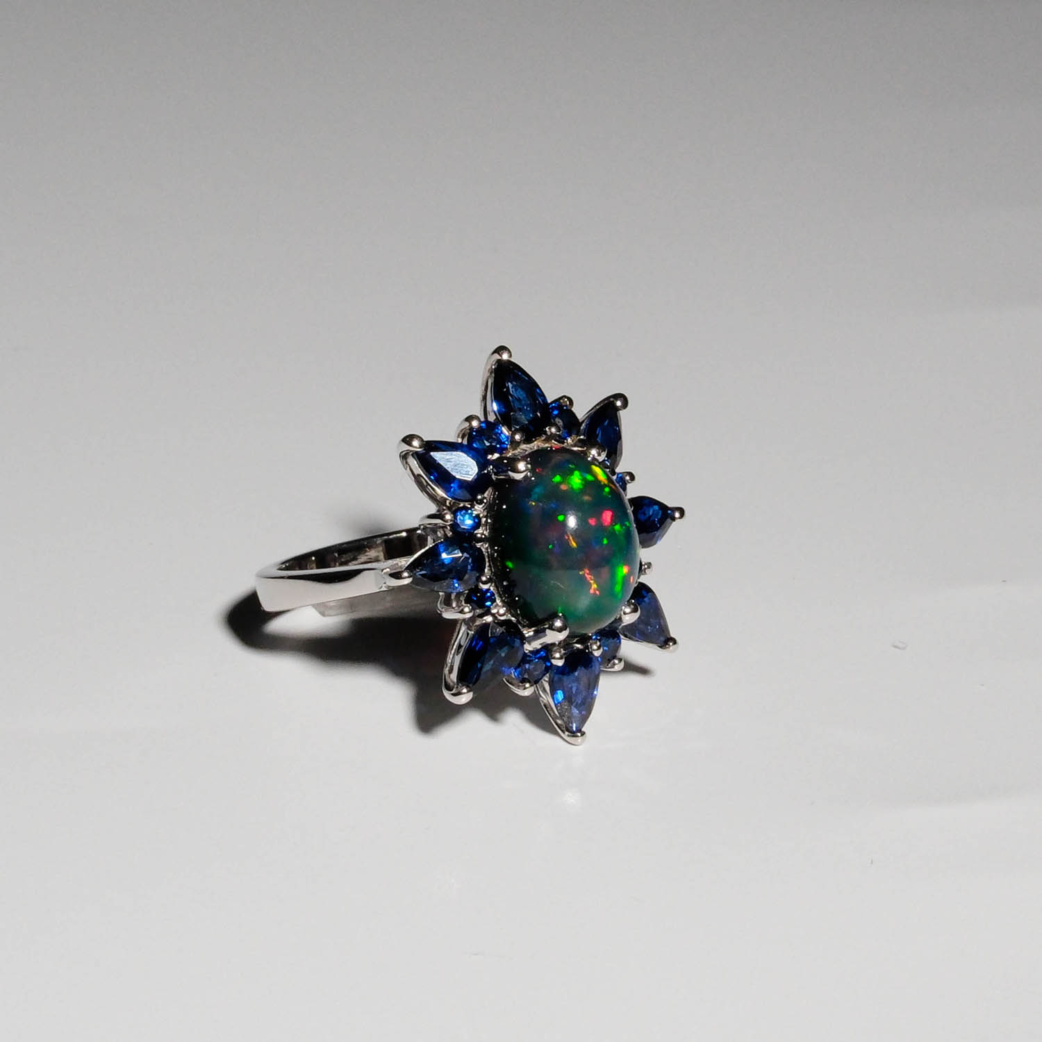 damen-ring-14-karat-gold-echter-opal-blauer-saphir-halo.jpg Damen Ring aus 14 Karat Gold mit feurigem grünem Opal und blauem Saphirkranz auf weißer Seide