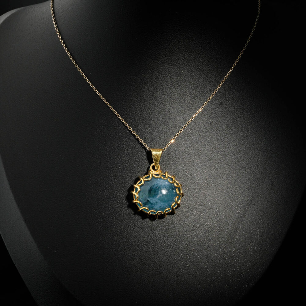 Natural oval cabochon deep blue aquamarine gemstone pendant necklace with braided gold plated 925 silver setting on white satin.