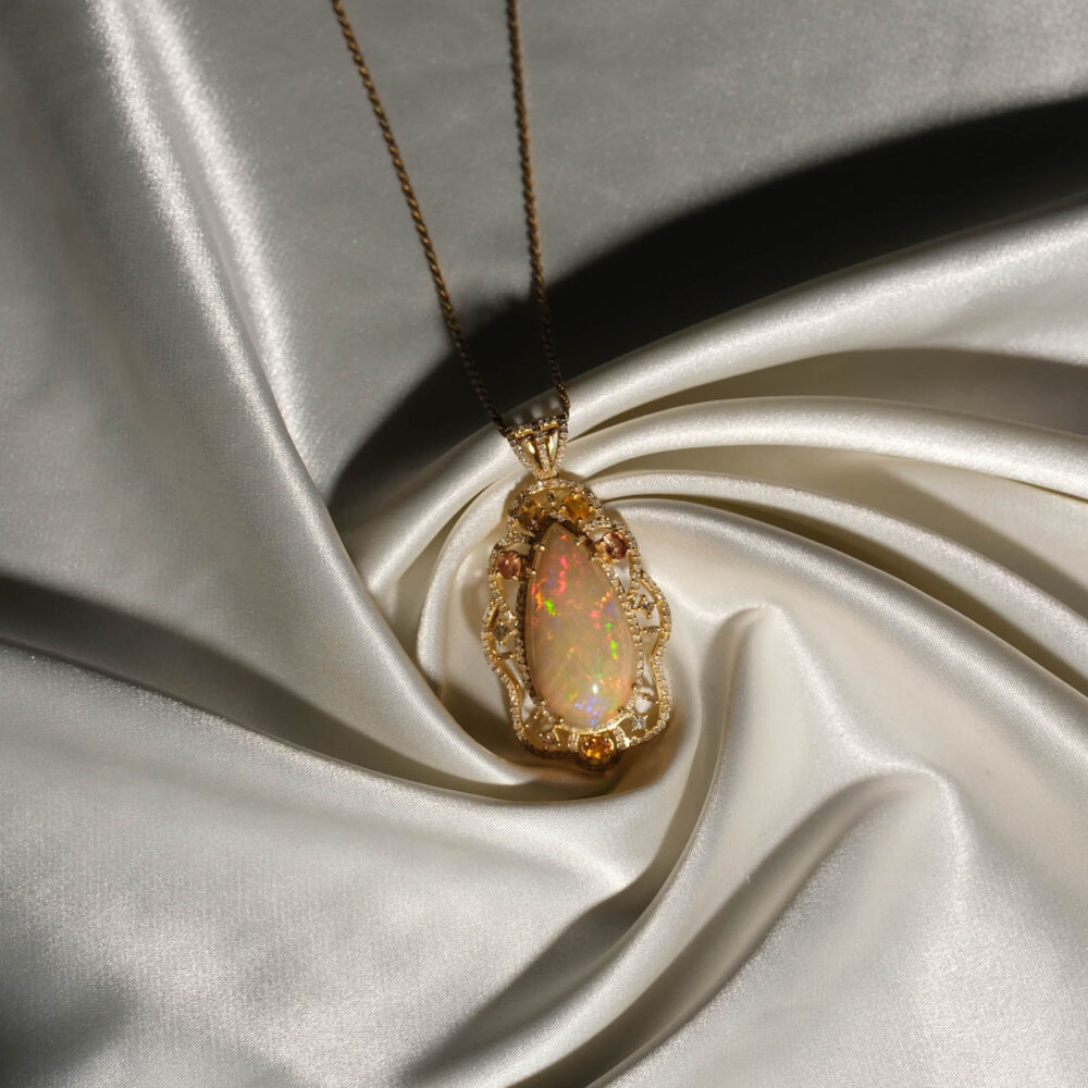 Natural teardrop cabochon fire opal pendant necklace with yellow sapphire and diamonds in gold plated 925 silver on white satin.