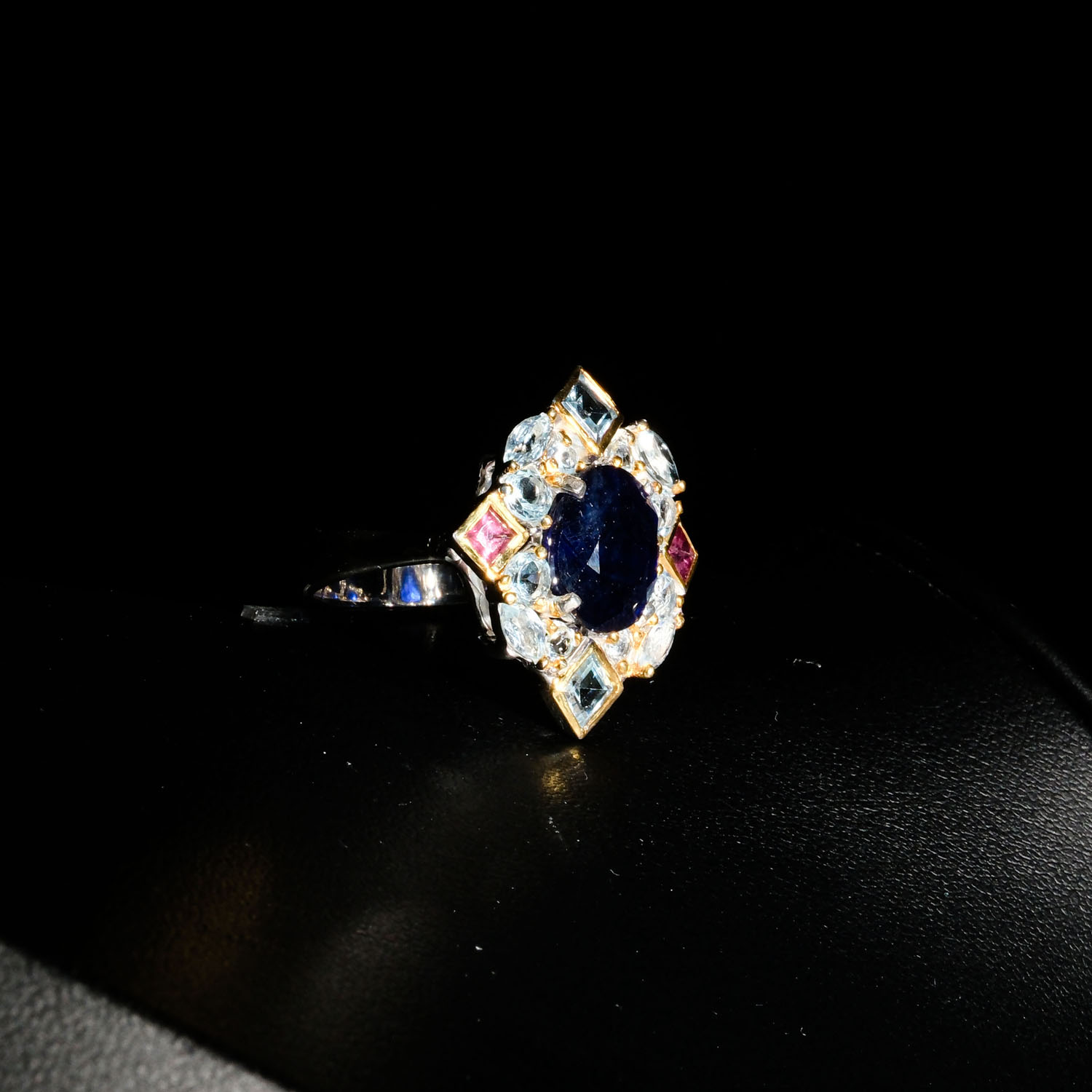 natural-oval-sapphire-blue-topaz-tourmaline-silver-ring.jpg Natural oval blue sapphire ring with blue topaz and pink tourmaline geometric halo in 925 sterling silver on white satin.