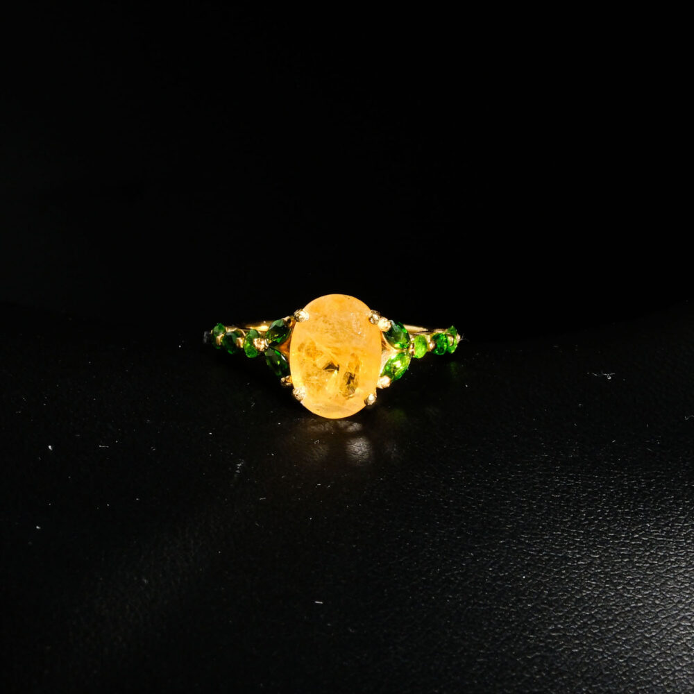 Genuine natural yellow sapphire oval gemstone surrounded by green tsavorite garnet halo yellow gold plated 925 sterling silver statement ring black background.