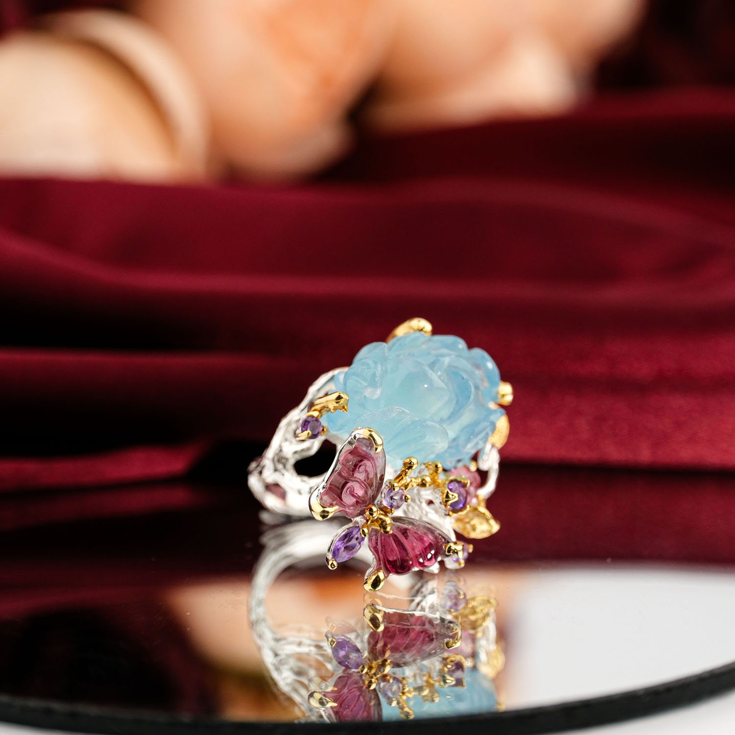 orijinal-carving-oyma-akuamarin-turmalin-pembe-opal-925-gumus-yuzuk.jpg Kırmızı kadife zemin üzerinde el oyması mavi çiçek akuamarin ve pembe kelebek turmalin taşlı sanatsal 925 gümüş kadın yüzük.