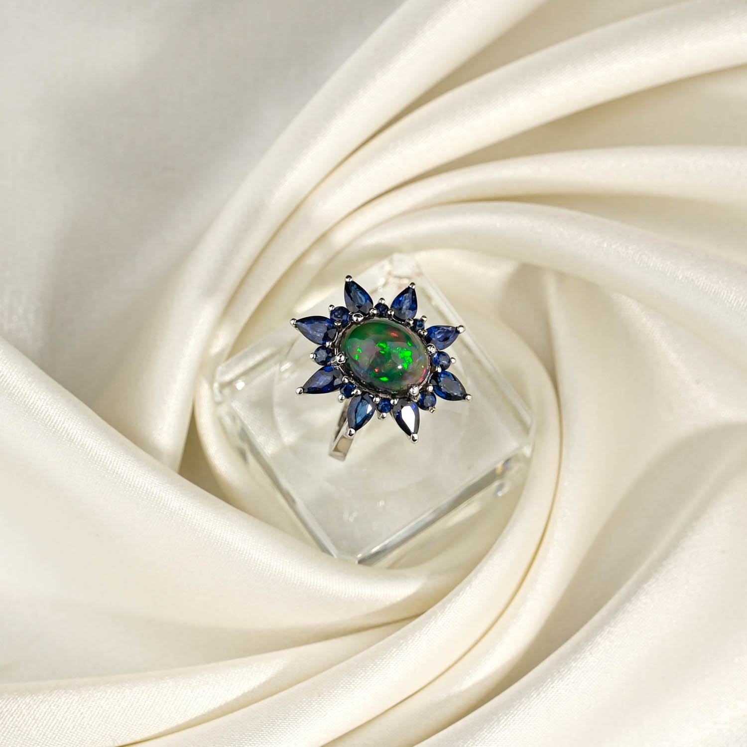 orijinal-opal-safir-tasli-14-ayar-altin-tasarim-kadin-yuzuk.jpg Beyaz saten kumaş üzerinde yeşil ateş parıltılı oval opal etrafında markiz lacivert safir dizili 14 ayar altın kadın yüzük